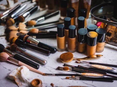 A variety of makeup brushes and foundation bottles arranged on a marble surface, showcasing beauty essentials.