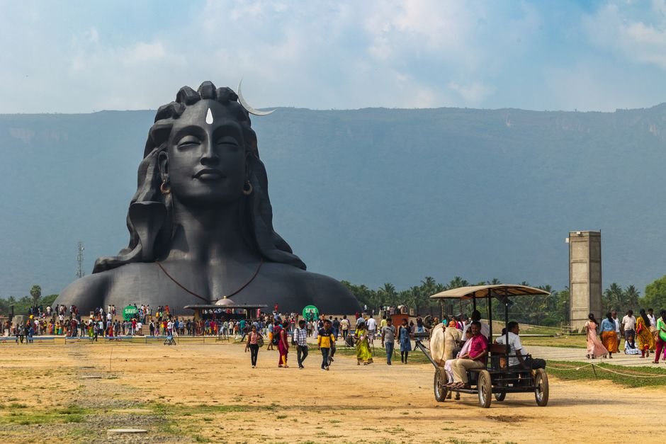 Coimbatore Corporation Demolishes Three-Storey Building on Encroached Land A vibrant scene at the Adiyogi Shiva statue with visitors and lush mountain backdrop in Booluvampatti, India.