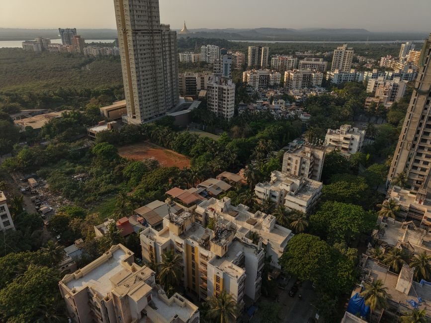 Mumbai Families Continue to Inhabit Landslide-Prone Homes Amidst Recurring Warnings Aerial shot of dense residential skyscrapers in Mumbai, surrounded by green areas at dusk.