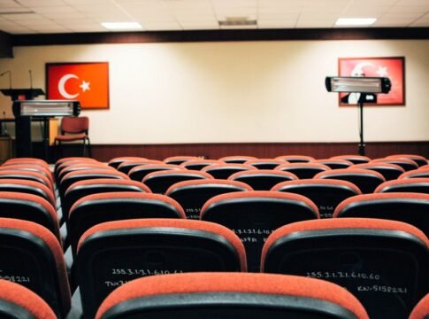 An empty conference room featuring red seats, a stage, and Turkish flags, ready for a meeting or presentation.