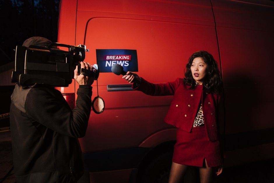Reporter Seeks Personal Best in Kenya’s Marathon Training Hub Asian female reporter with cameraman conducting a nighttime news broadcast beside a news van.