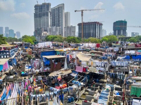 Colorful laundry drying at Mumbai Dhobi Ghat with city skyline in background.