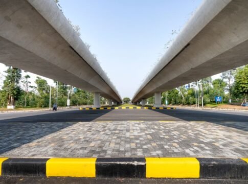 Concrete elevated highways over asphalt road between lush greenery in suburb under blue sky Concrete elevated highways over asphalt road between lush greenery in suburb under blue sky