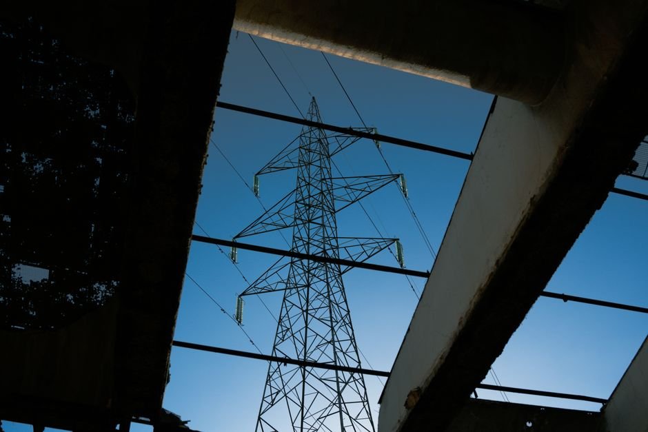 US Heatwave Pushes Power Grid to Brink, Threatening Blackouts Electric tower framed by industrial ruins against a blue sky.