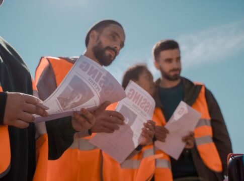 Group of volunteers in orange vests distributing missing person flyers outdoors. Group of volunteers in orange vests distributing missing person flyers outdoors.