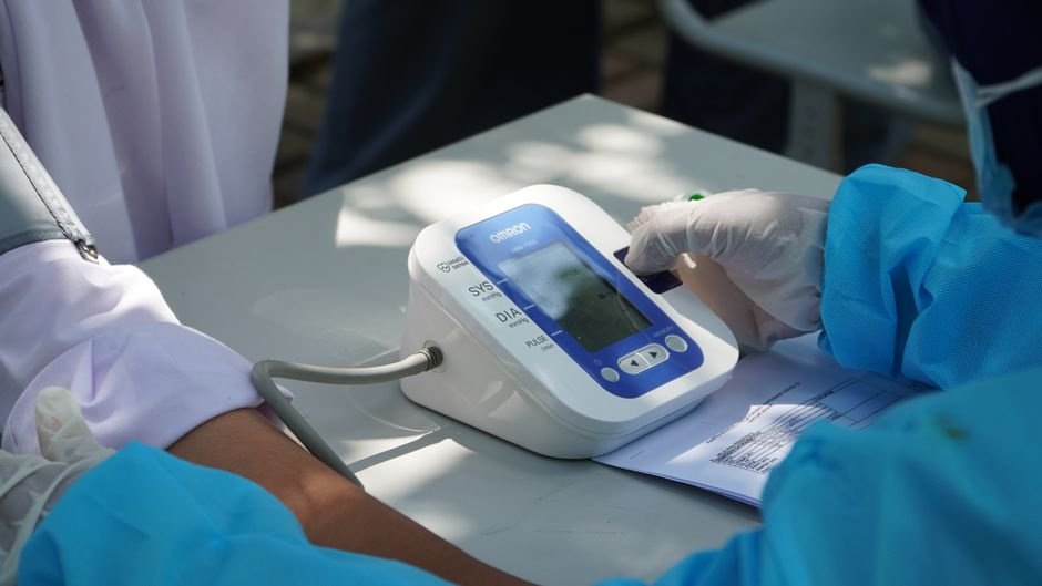 Andhra Pradesh Organisation Urges Enhanced Disease Surveillance Amidst COVID-19 Resurgence Healthcare worker checking patient's blood pressure with a digital device outdoors.