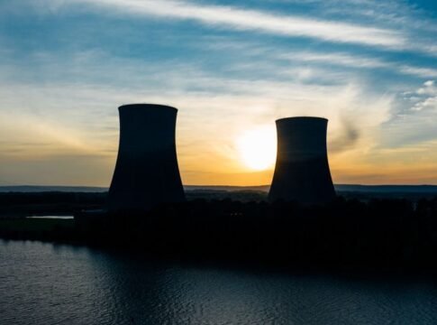 Identical cooling tower silhouettes on power plant near rippled river under colorful cloudy sky at sundown Identical cooling tower silhouettes on power plant near rippled river under colorful cloudy sky at sundown