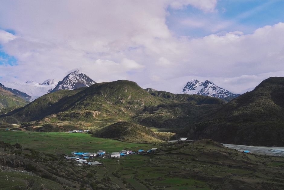 Punjab’s Ghulal Village: Where Sikh History and Education Intertwine Picturesque village nestled in lush mountains with snow-capped peaks under a cloudy sky.