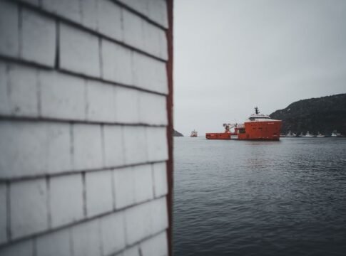 Red ship on Newfoundland bay with rugged coastline and overcast sky. Red ship on Newfoundland bay with rugged coastline and overcast sky.