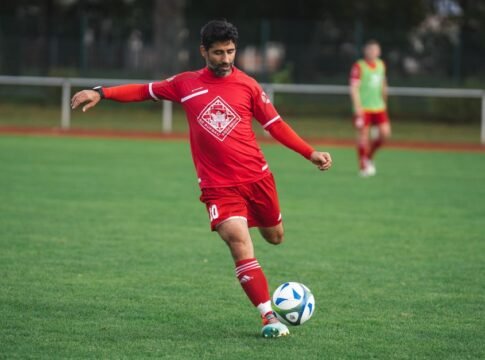 Soccer player in red uniform kicks ball on a green field. Action shot outdoors. Soccer player in red uniform kicks ball on a green field. Action shot outdoors.
