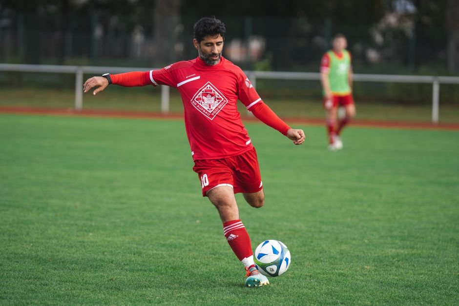 Soccer player in red uniform kicks ball on a green field. Action shot outdoors.