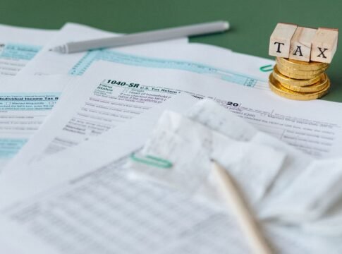 Stack of tax forms and coins with a 'TAX' stamp, symbolizing finance and accounting. Stack of tax forms and coins with a 'TAX' stamp, symbolizing finance and accounting.