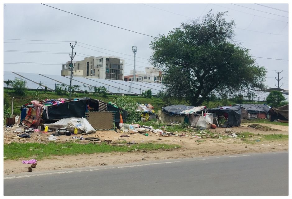 Pune Engineer Illuminates Lives with Free Solar Electricity Initiative Street scene showing makeshift homes near solar panels in Vadodara, India.