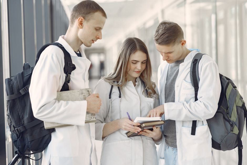 Tamil Nadu Health Minister Alleges Private Medical Colleges Exploited Loopholes for Deemed Status Three medical students in a hallway discussing notes, fostering teamwork and learning.