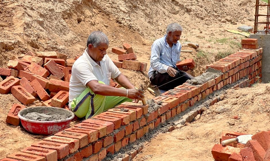 Two men laying bricks at a construction site in Rasulpur, India.