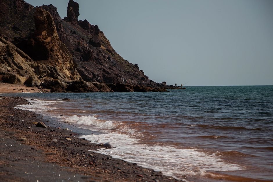 Middle East Shipping Risks Escalate, Threatening Global Oil Routes Waves crash on the rocky shore of Hormoz Island, Iran with clear blue skies.