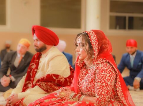 A bride and groom in traditional attire during an Indian wedding ceremony inside a venue.