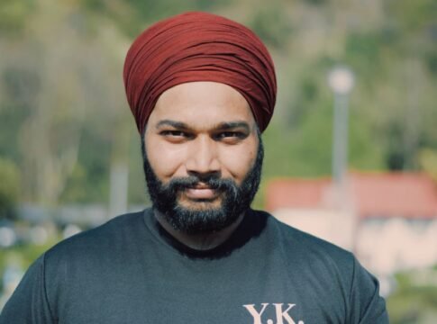 A cheerful man wearing a red turban and black t-shirt enjoys a sunny day outdoors.