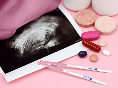 A closeup of pregnancy tests and an ultrasound with supplements on a pink background.