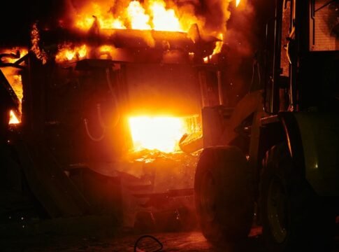A dramatic industrial fire with flames engulfing machinery in a nighttime scene.