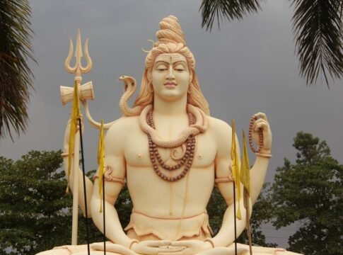 A grand Shiva statue amidst palm trees with a dramatic cloudy backdrop.
