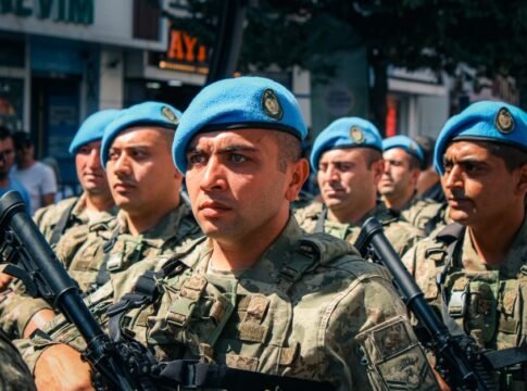 A group of soldiers in blue berets marching during a daytime military parade in the city.