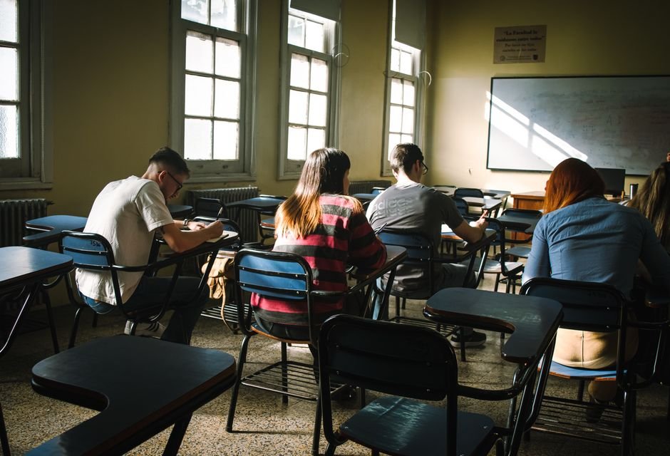 Allegations of Widespread Cheating Emerge in Mexico’s UNAM College Entrance Exam A group of students focused on writing in a sunlit classroom with desks and windows.