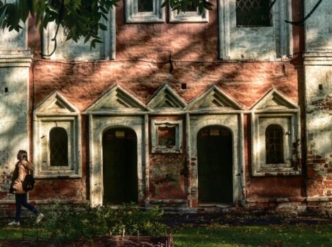 A historic monastery facade in Russia with sunlight casting shadows, a woman walking by. A historic monastery facade in Russia with sunlight casting shadows, a woman walking by.
