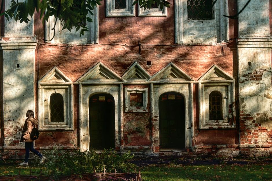 Russia Explores Overland Rail Link to India via Central Asia A historic monastery facade in Russia with sunlight casting shadows, a woman walking by.