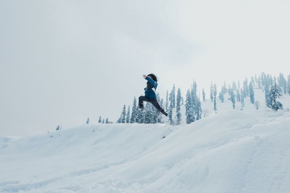 Jammu and Kashmir: Hundreds Attend Condolence Meeting for Engineer Anwar Ashai A man leaps across a snow-covered hillside against a backdrop of trees in Gulmarg.
