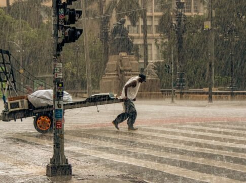 A man pulling a cart across a wet city street during a heavy rainstorm, showcasing resilience.