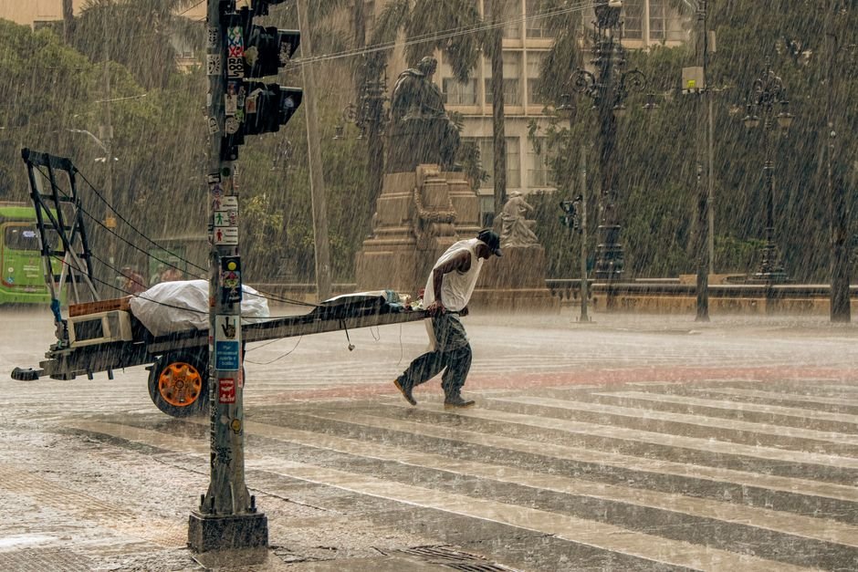 Himachal Pradesh: Torrential Rains Wreak Havoc, Disrupting Over 100 Roads and 200 Water Schemes A man pulling a cart across a wet city street during a heavy rainstorm, showcasing resilience.