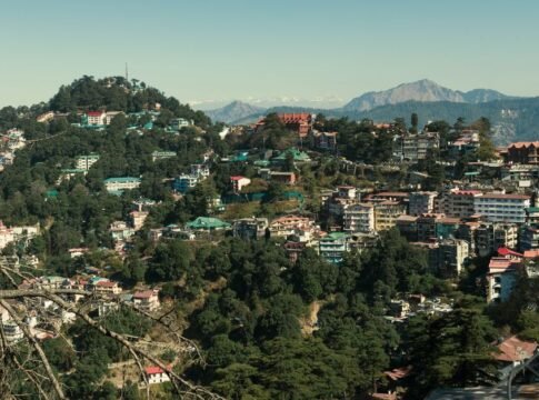 A picturesque view of a hill town surrounded by lush greenery and majestic mountains in the background.