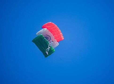A skydiver descends with an Indian flag parachute against a bright blue sky, symbolizing adventure and patriotism.