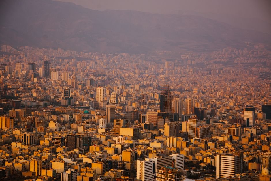US Strike Kills Family of Three, Wounds Two Children in Iran’s Qeshm Island Residential Area A sprawling view of Tehran's urban landscape with mountains in the background at sunset.
