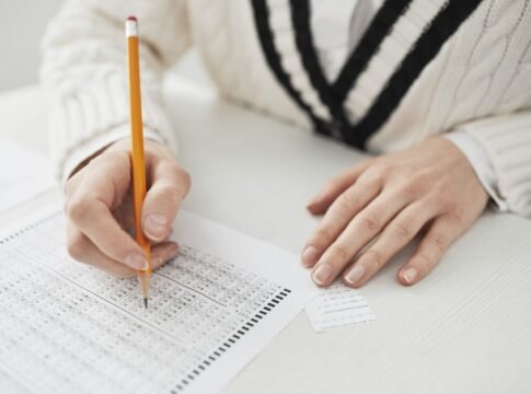 A student writing answers on a multiple-choice exam sheet at a desk. A student writing answers on a multiple-choice exam sheet at a desk.