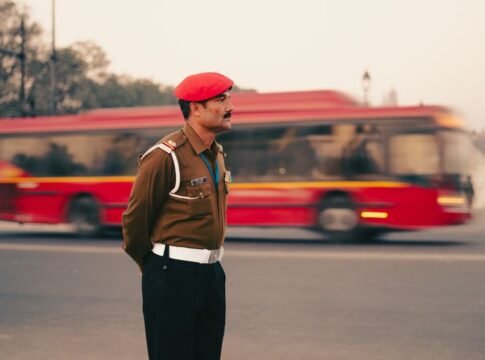 A traffic officer in a red beret stands in New Delhi, with a blurred red bus in the background. A traffic officer in a red beret stands in New Delhi, with a blurred red bus in the background.