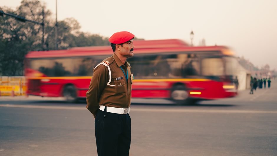 Delhi Police Conduct Mock Drills in Kalkaji Mandir, Nehru Place Ahead of Independence Day A traffic officer in a red beret stands in New Delhi, with a blurred red bus in the background.