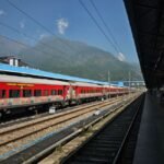 A vibrant red train at an outdoor station with scenic mountain backdrop, ideal for travel themes.