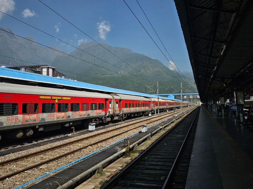 Jammu: Sabarmati-Jammu Tawi Express Extended to Katra A vibrant red train at an outdoor station with scenic mountain backdrop, ideal for travel themes.
