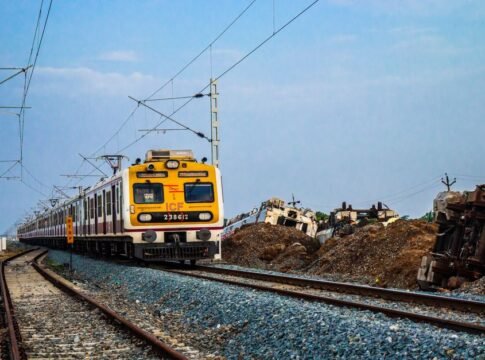 A yellow electric train traveling on curved tracks outside with clear blue sky in the background.