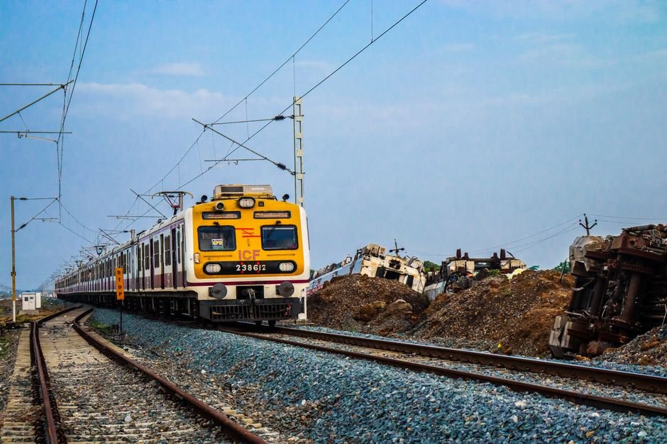 Bengaluru Suburban Rail Corridors Face Persistent Land Acquisition Delays A yellow electric train traveling on curved tracks outside with clear blue sky in the background.
