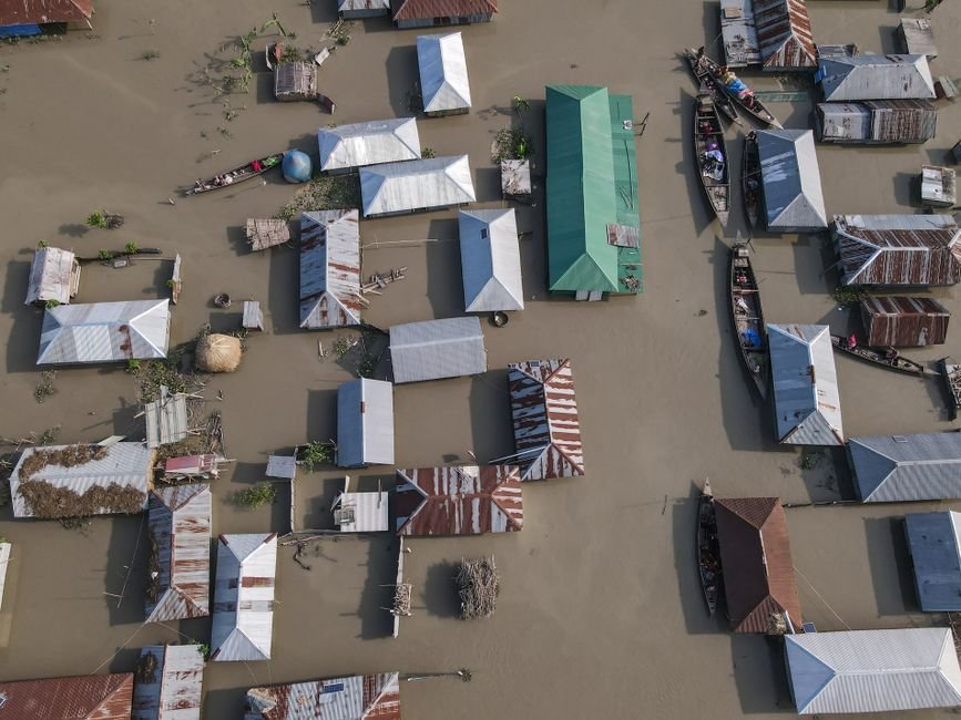 American Survivor Recounts Terrifying Nepal Flood Aerial perspective of a village submerged in floodwaters, highlighting tin-roofed houses and boats.