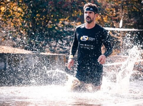 Athlete running through water splash during outdoor obstacle race.