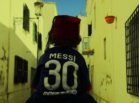Back view of a person on a Tunis street wearing a fez and Messi jersey.