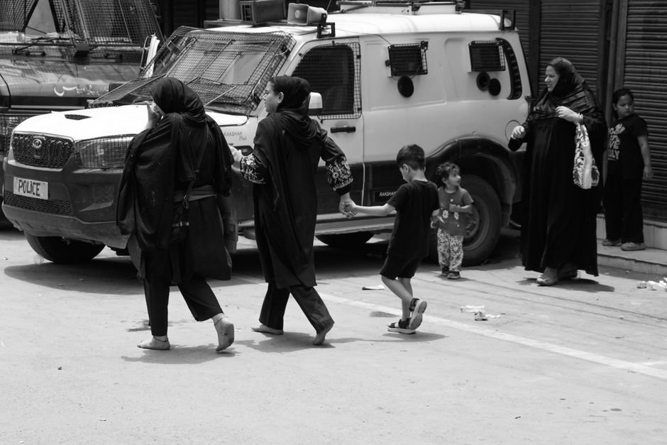 Kashmir: Robust Security Setup in Place for Independence Day, Says IGP Birdi Black and white image capturing people walking past a police vehicle in an urban setting.