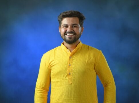 Cheerful man wearing traditional yellow kurta posing against a vibrant blue background.