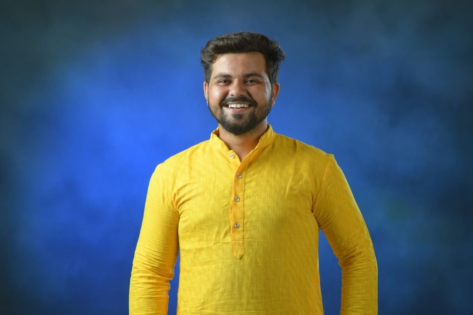 Delhi Court Issues Notice to AAP Leader in Defamation Case Cheerful man wearing traditional yellow kurta posing against a vibrant blue background.
