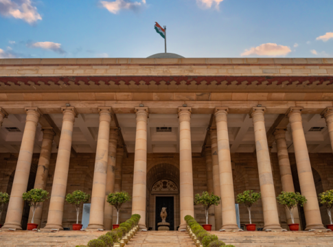 Government building in New Delhi featuring columns and an Indian flag under a vibrant sky.