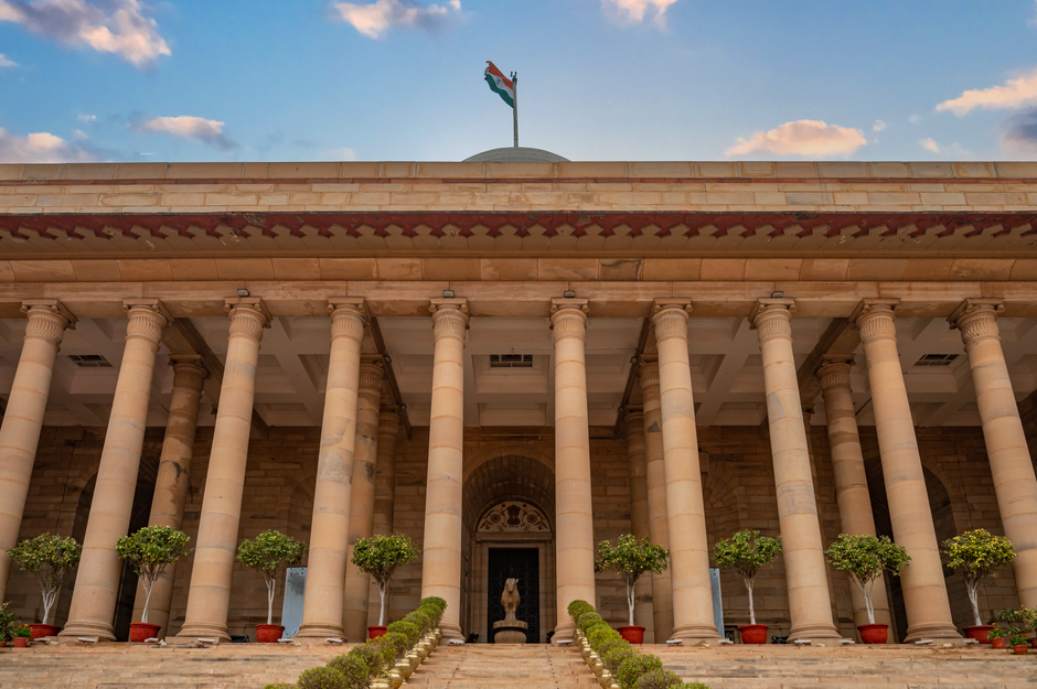 Jammu and Kashmir: NITI Aayog Delegation Urges Enhancement of Education, Health Sectors Government building in New Delhi featuring columns and an Indian flag under a vibrant sky.